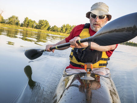 senior male is paddling a fast racing sea kayak  with a wing paddle on a calm lake, Fort Collins, Coloradoの写真素材