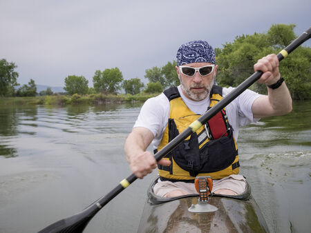 senior male paddler training in a narrow fast racing kayak on a lake, focus on paddler's faceの写真素材