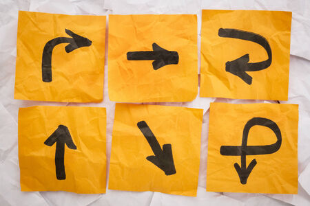 confusing directions concept - a variety of arrows on crumpled, orange sticky notesの写真素材