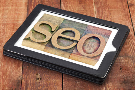 search engine optimization - SEO acronym in letterpress wood type  on a digital tablet against red barn woodの写真素材