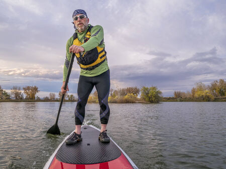senior paddler in life jacket enjoying stand up paddling on lake, fall scenery in Fort Collins, Coloradoの写真素材