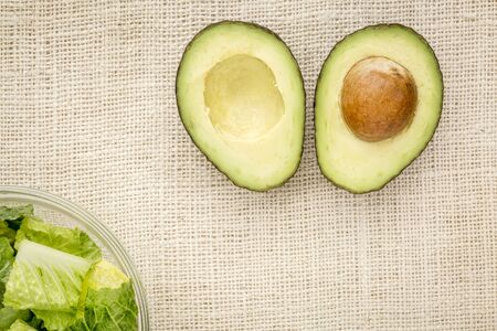 halved avocado and a bowl of romaine lettuce against burlap canvas