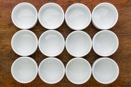a dozen of empty white ceramic tasting bowls against rustic woodの写真素材