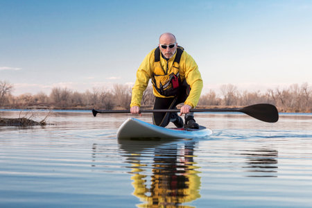 Senior male on stand up paddling (SUP) board. Early spring on calm lake in Colorado.のeditorial素材