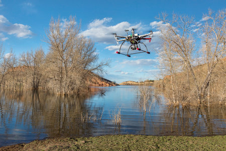 FORT COLLINS, CO, USA, March 30,  2015:  DJI F550 Flame Wheel  hexacopter drone is  flying with a camera in early spring over  lake.with submerged cottonwood trees.のeditorial素材
