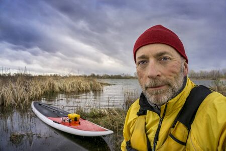 senior paddler in life jacket with his paddleboard and lake in background, early spring scenery with stormy sky in Coloradoの写真素材