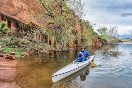 a senior paddler in an decked expedition canoe approaching rocky sandstone shore - Horsetooth Reservoir near Fort Collins, Coloradoの写真素材