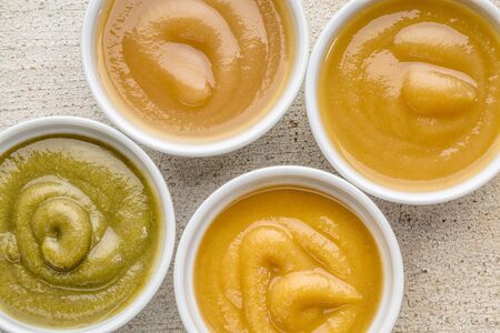 organic fruit and vegetable baby food or snack (apple, pea, spinach, corn, sweet potato, grape, peach) - top view of ceramic bowlsの写真素材