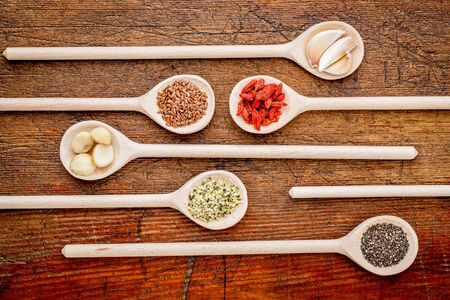 superfood abstract (garlic cloves, goji berry, chia, hemp, flax seeds, macadamia,nuts) - top view of wooden spoons against rustic grunge woodの写真素材