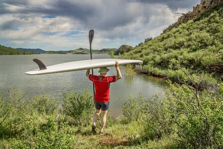 male paddler carrying a stand up paddleboard and a paddle on a sunny summer day - Horsetooth Reservoir, Fort Collins, Coloradoの写真素材