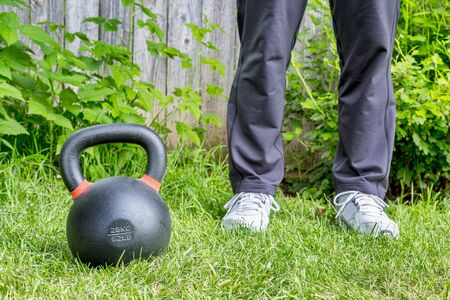 fitness workout with a heavy iron competition kettlebell (62lb/28 kg) on green grass in backyard - outdoor training conceptの写真素材