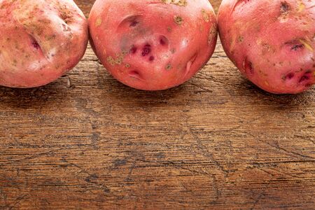 a row of three red potatoes on rustic wood with a copy spaceの写真素材