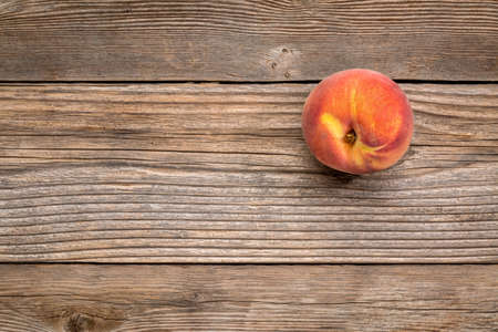single fresh peach fruit on weathered grained wood with a copy spaceの写真素材