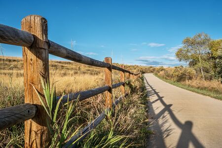 wooden fence with a shadow and a  bike trail  - Poudre River Trail in northern Colorado near Windsor. It is a  paved path  extending more than 20 miles between Timnath and Greeley.の写真素材