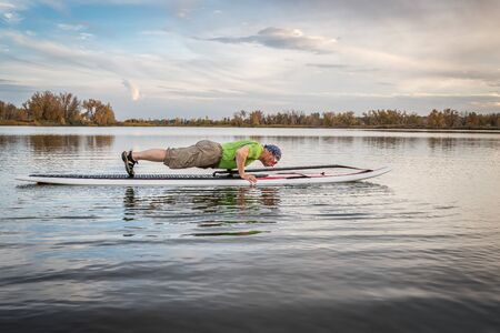 senior male doing pushups and planks for warming up on a paddleboard before paddling workout on a...