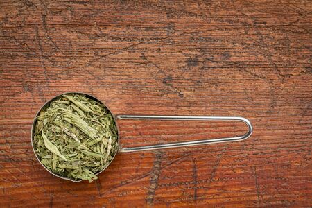 stevia dried leaves in a metal measuring scoop against rustic wood - natural sweetener, sugar substituteの写真素材