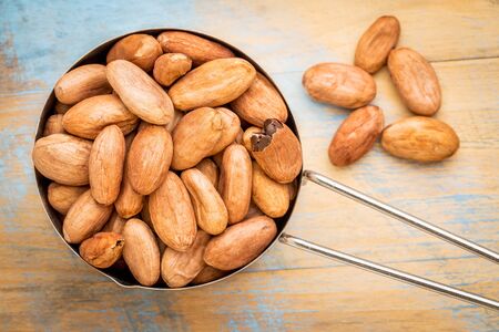 metal measuring scoop of raw organic cacao beans  against grunge wood tableの写真素材