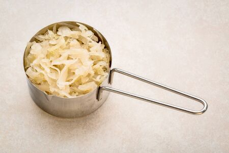 metal measuring scoop of sauerkraut against ceramic tile - healthy eating concept (probiotic food)