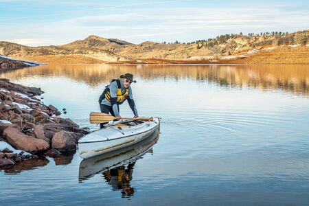 senior male paddler with his decked expedition canoe on a shore  of Horsetooth Reservoir near Fort Collins in northern Colorado, winter sceneryの写真素材