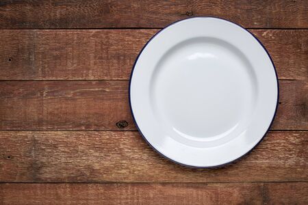 empty white metal enamel plate against rustic wood with a copy spaceの写真素材