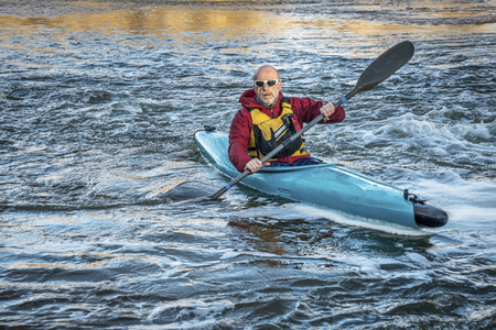 senior male paddling a whitewater kayak on a turbulent riverの写真素材