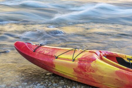 Bow of whitewater kayak on a river shore with a rapid in backgroundの写真素材
