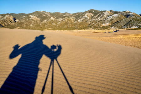 a photographer shooting - a shadow of a photographer with a camera and tripod on a sand duneの写真素材