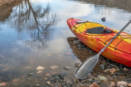 colorful river kayak with a paddle on rocky lake shore with a tree reflection - recreation conceptの写真素材