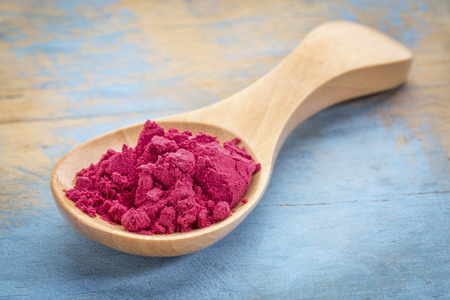 aronia berry powder on a wooden spoon against blue painted grunge woodの写真素材