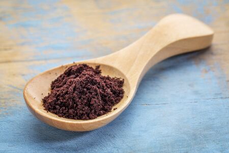 acai berry powder on a wooden spoon against blue painted grunge woodの写真素材