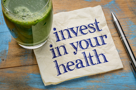invest in your health advice or reminder - handwriting on a napkin with a glass of fresh, green, vegetable juiceの写真素材