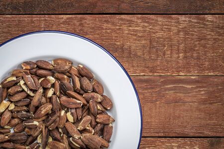 roasted pili nuts grown in Philippines, top view of nuts on white metal plate against  a rustic abrn woodの写真素材