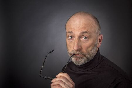 60 years old  man with a beard and reading glasses -  a headshot against a black backgroundの写真素材