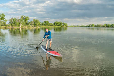 senior male paddler on a paddleboard, lake in northern Colorado with an early summer scenery