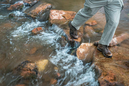 legs of a male hiker crossing mountain creek in Colorado foothillsの写真素材
