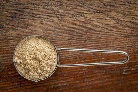 maca root powder on a metal measuring scoop against rustic weathered wood