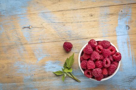 a bowl of red raspberries fresh from a garden on wood with a copy space