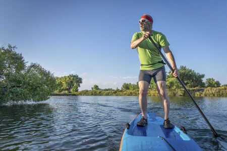muscular, senior male paddling  a stand up paddleboard on a lake in Colorado