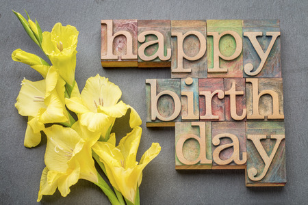 happy birthday greeting card - word abstract in letterpress wood type with a yellow gladiola flower against gray slate stone backgroundの写真素材