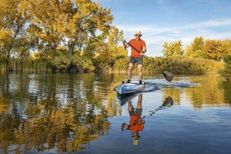 Senior male paddler enjoys workout on his racing stand up paddleboard in fall colors on lake in Coloradoの写真素材