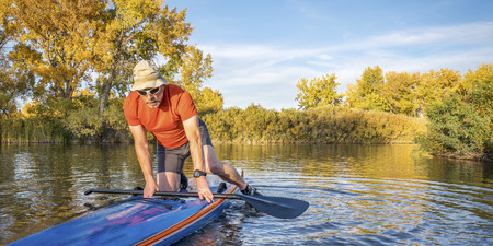 Senior male paddler is starting  workout on his racing stand up paddleboard in fall colors on lake in Coloradoの写真素材