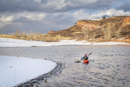winter kayaking in Colorado - senior male paddler in a red whitewater kayak on  Horsetooth Reservoir near Fort Collinsの写真素材