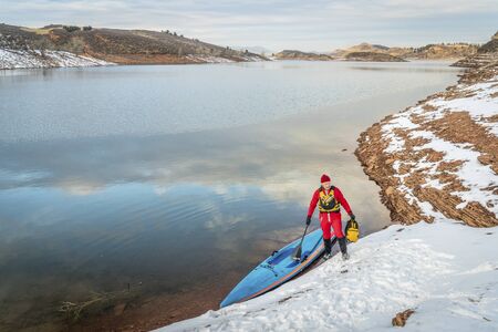 senior male paddler in drysuit and stand up paddleboard on lake in Colorado, winter sceneryの写真素材