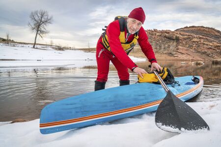 senior male paddler in drysuit and a racing stand up paddleboard on lake in Colorado, winter sceneryの写真素材