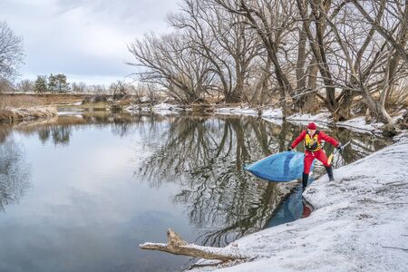 winter stand up paddling on the Poudre River in Fort Collins, northern Colorado -senior male paddler is launching his board from an icy shoreの写真素材