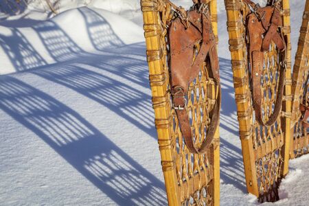 detail of vintage wooden Bear Paw  snowshoes with leather binding in snow with shadowの写真素材