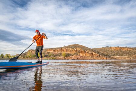 A senior male paddling on a stand up paddleboard on a calm mountain lake - Horsetooth Reservoir near...