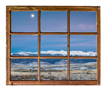 full moon over snowy Medicine Bow Mountains, North Park near Walden, Colorado as seen through vintage sash windowの写真素材