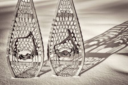 vintage wooden Huron snowshoes with leather binding in snow with shadow, retro sepia toningの写真素材
