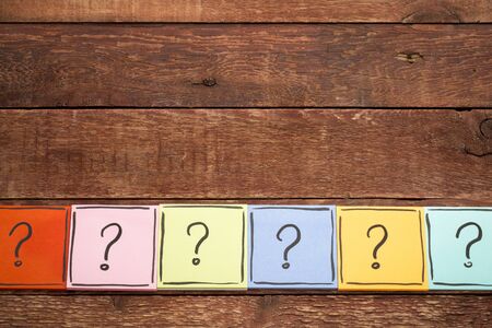 question mark concept  - handwriting in black ink on colorful sticky notes against rustic wood with...